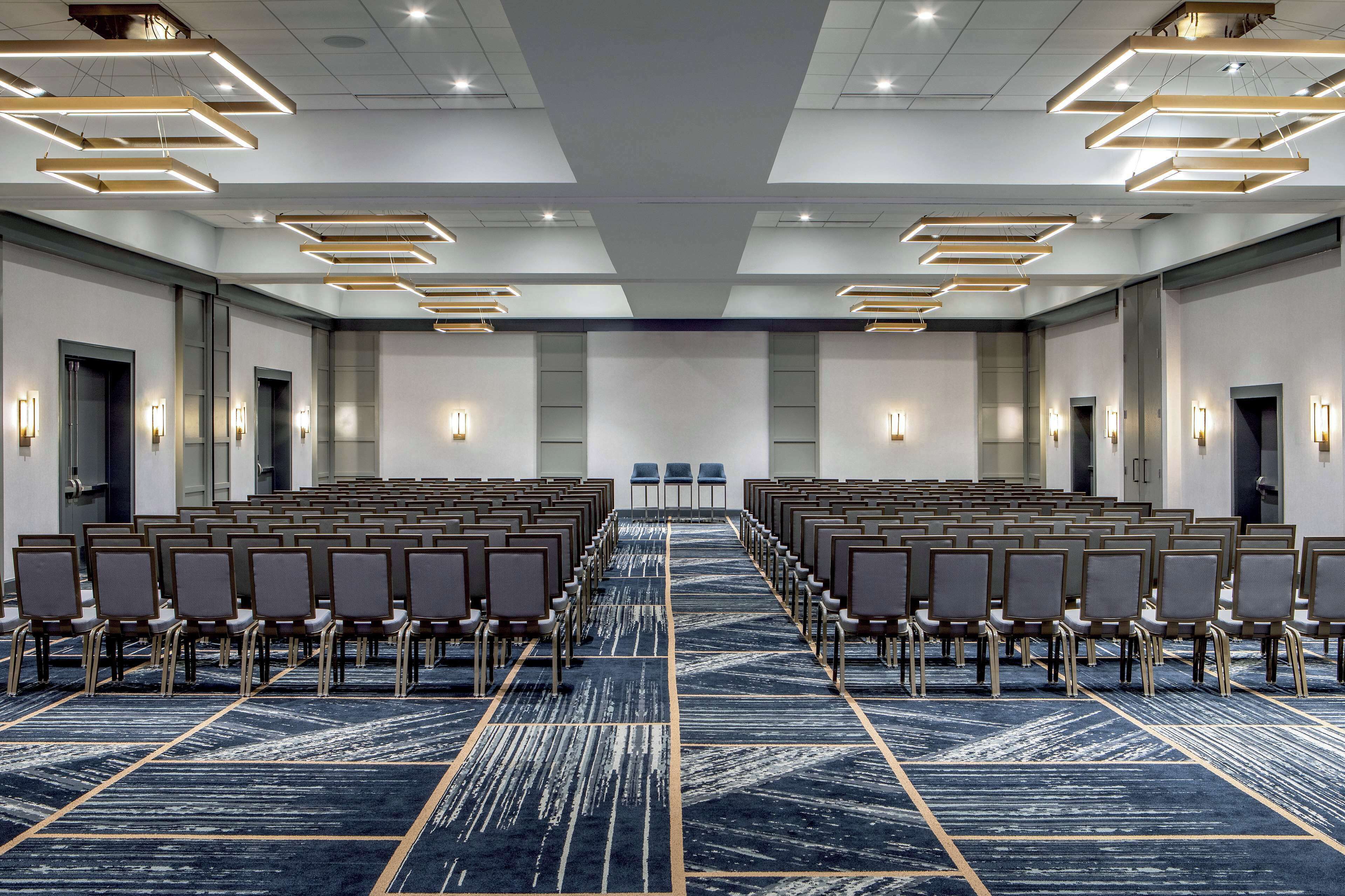 A conference room with rows of chairs, a patterned carpet, and modern lighting fixtures.
