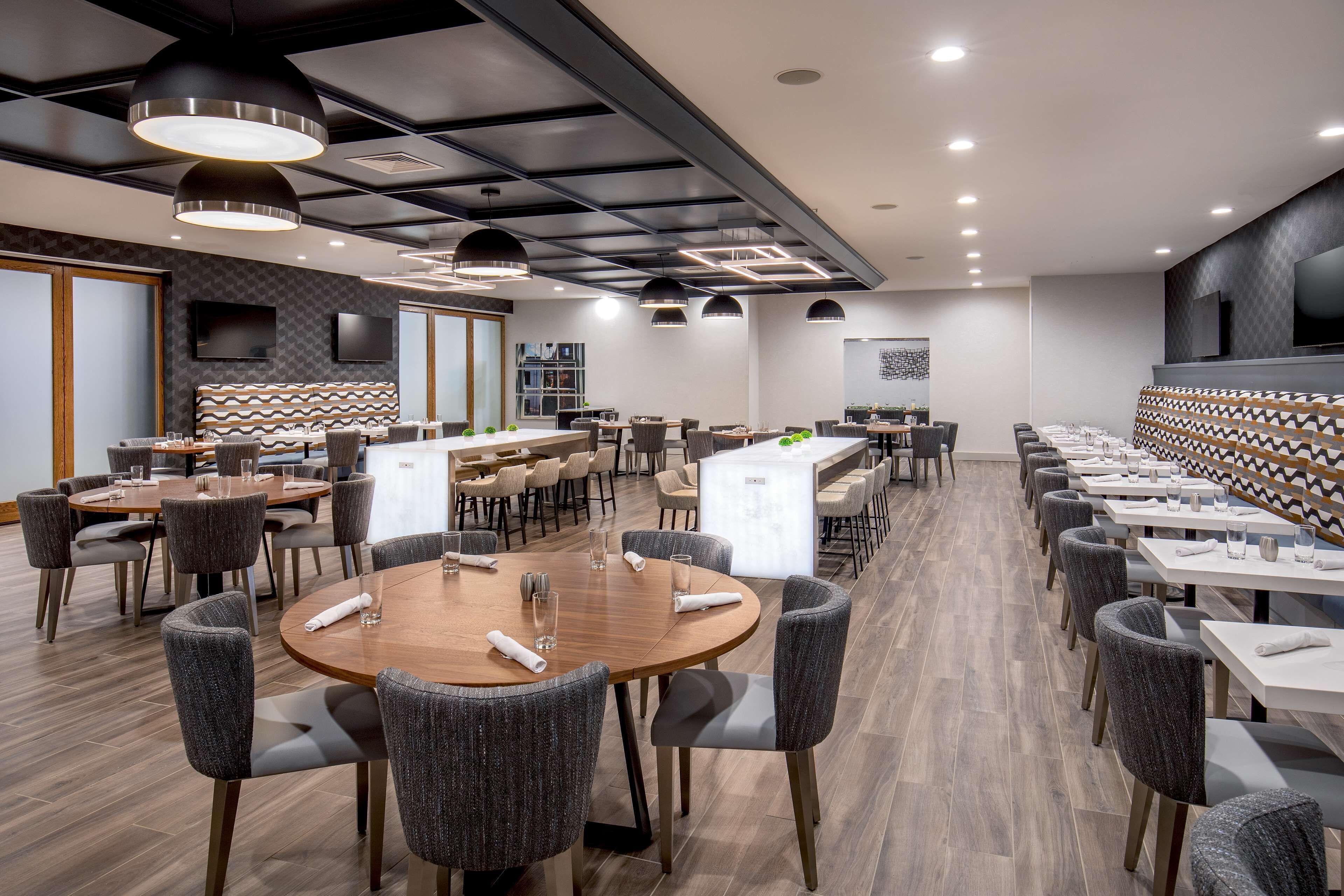 Un comedor moderno con mesas redondas, sillas tapizadas en gris e iluminación colgante.
