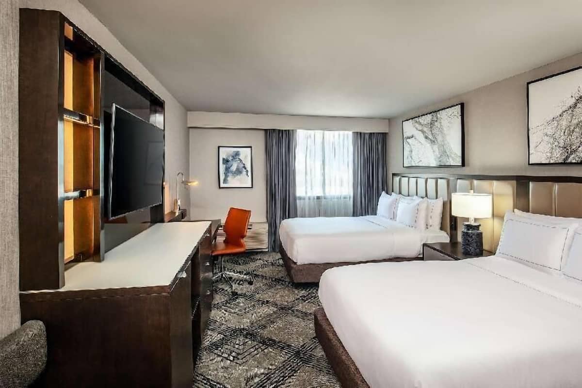 Une chambre d’hôtel avec deux lits, un bureau, une télévision et des œuvres d’art accrochées aux murs.