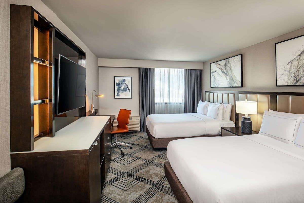 Une chambre d’hôtel équipée d’un bureau, de deux lits, d’une télévision et d’œuvres d’art accrochées aux murs.