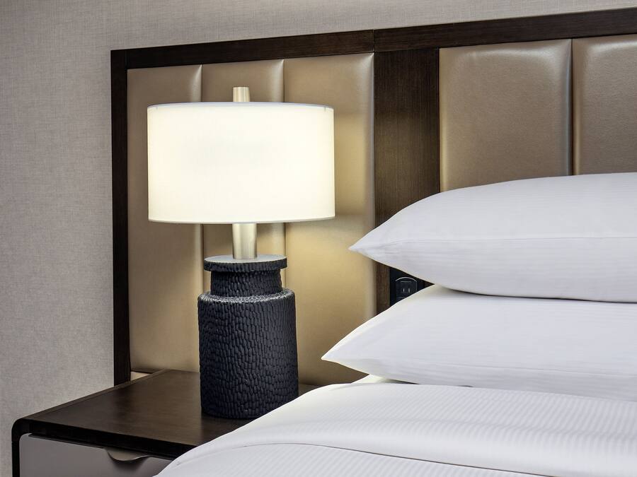 A neatly made bed with white linens and a lamp on a bedside table.