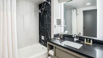 Un baño moderno con bañera, un espejo grande y un salpicadero de mármol negro.