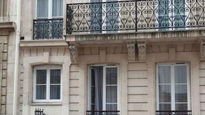 Um edifício de vários andares com varandas ornamentadas, uma entrada central com portão de ferro forjado e uma placa indicando um hotel.