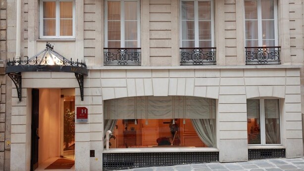 Fachada de hotel com estilo arquitetônico clássico, destacando uma entrada central com toldo, várias janelas com grades de ferro decorativas e a placa do hotel visível.
