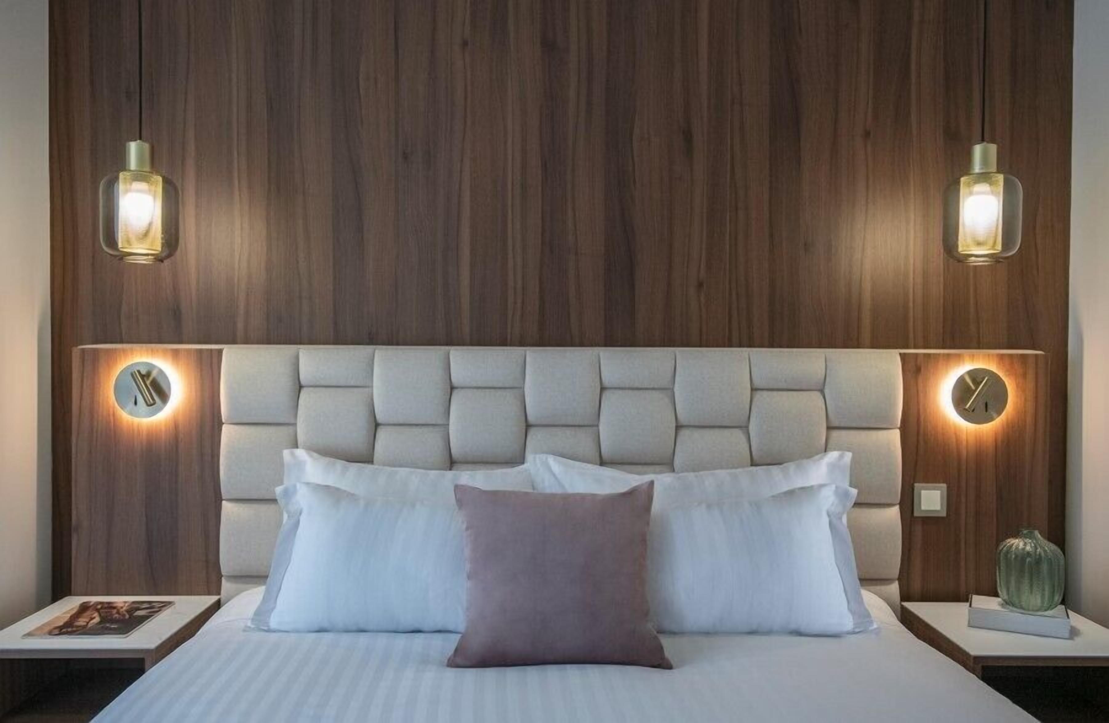 A bedroom with a tufted headboard, two bedside tables with lamps, a bed with pillows, and a wall clock.