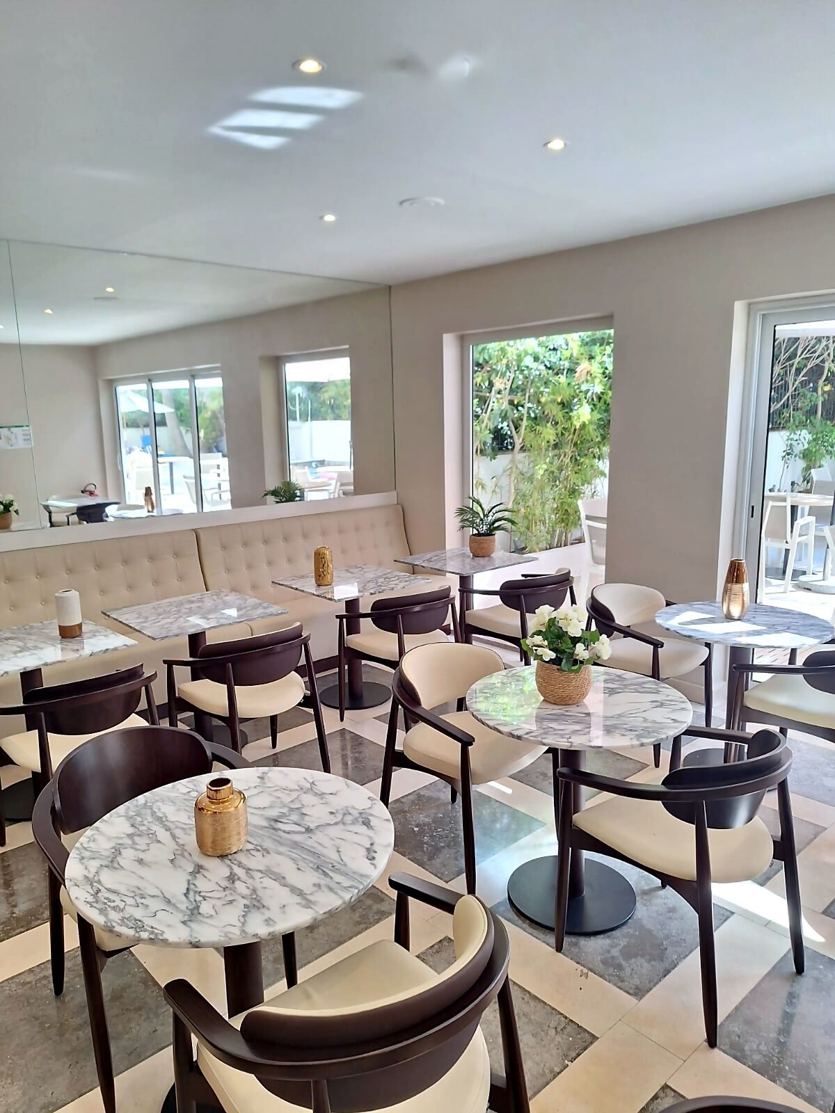 A modern indoor seating area with round tables and cushioned chairs, large windows with a view of greenery, and a neutral color palette.