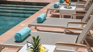 A poolside area with lounge chairs and towels, a table with a pineapple and a drink, and a clear view of the pool. - Le Cetai Cannes Beach Hotel (Cannes)