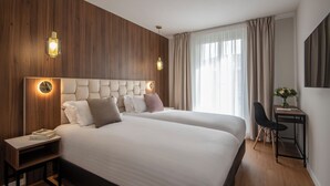 A hotel room with a large bed, wooden paneling on the walls, a desk with a chair, and a large window with curtains. - Le Cetai Cannes Beach Hotel (Cannes)