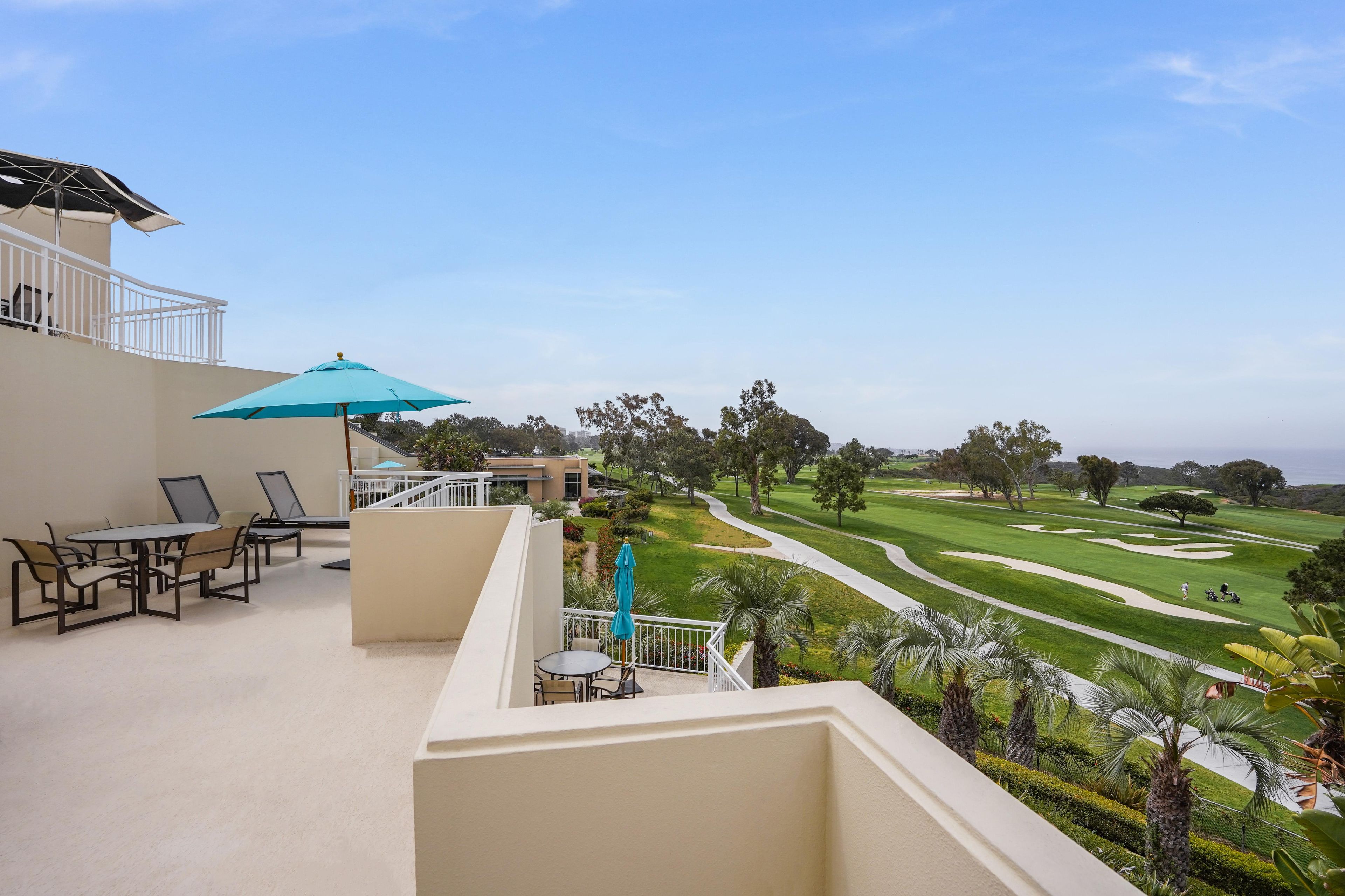 Un balcón con mesa y sillas, una sombrilla azul y vistas a un campo de golf.