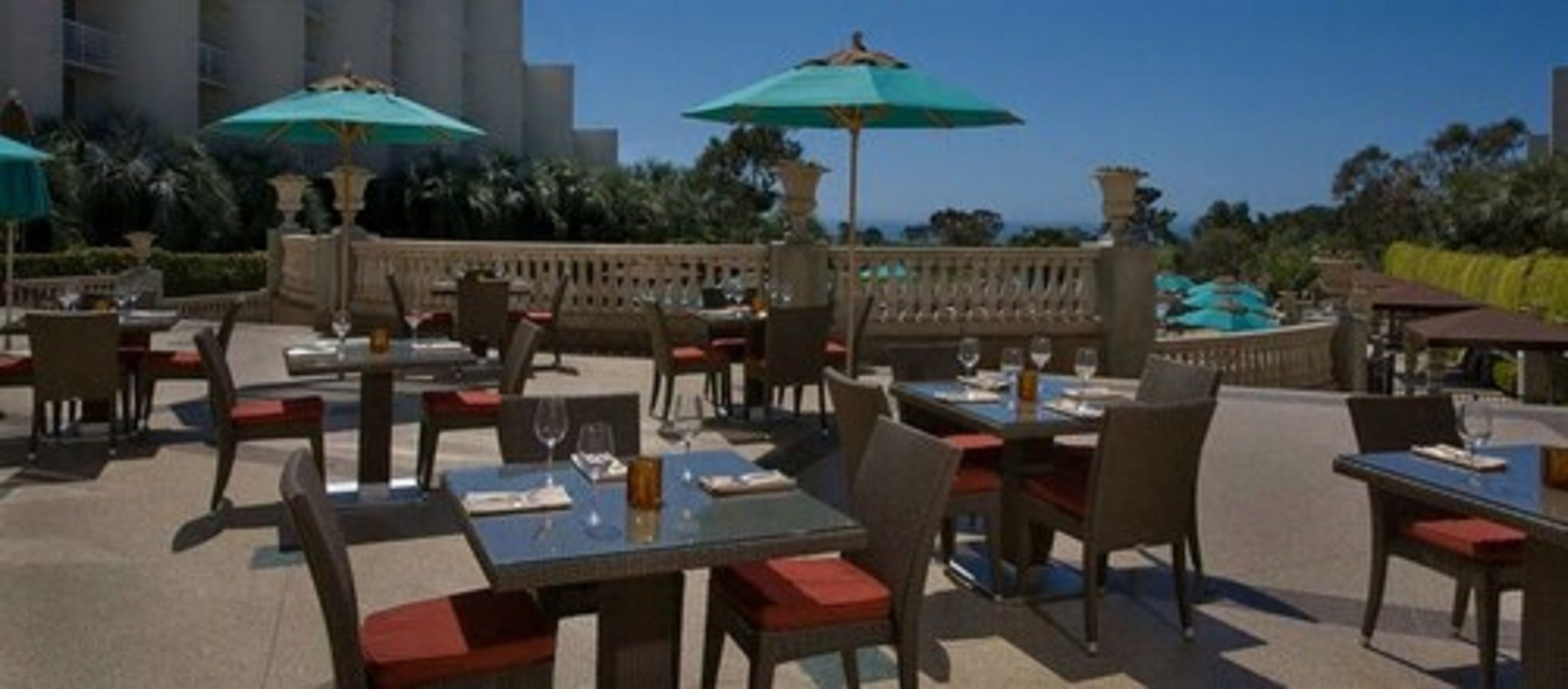 Un área de comedor al aire libre con mesas, sillas, sombrillas y vista al océano.