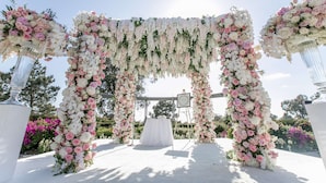 An outdoor wedding arch with white and pink flowers, a white table, and a clear sky. - Hilton La Jolla Torrey Pines (La Jolla)