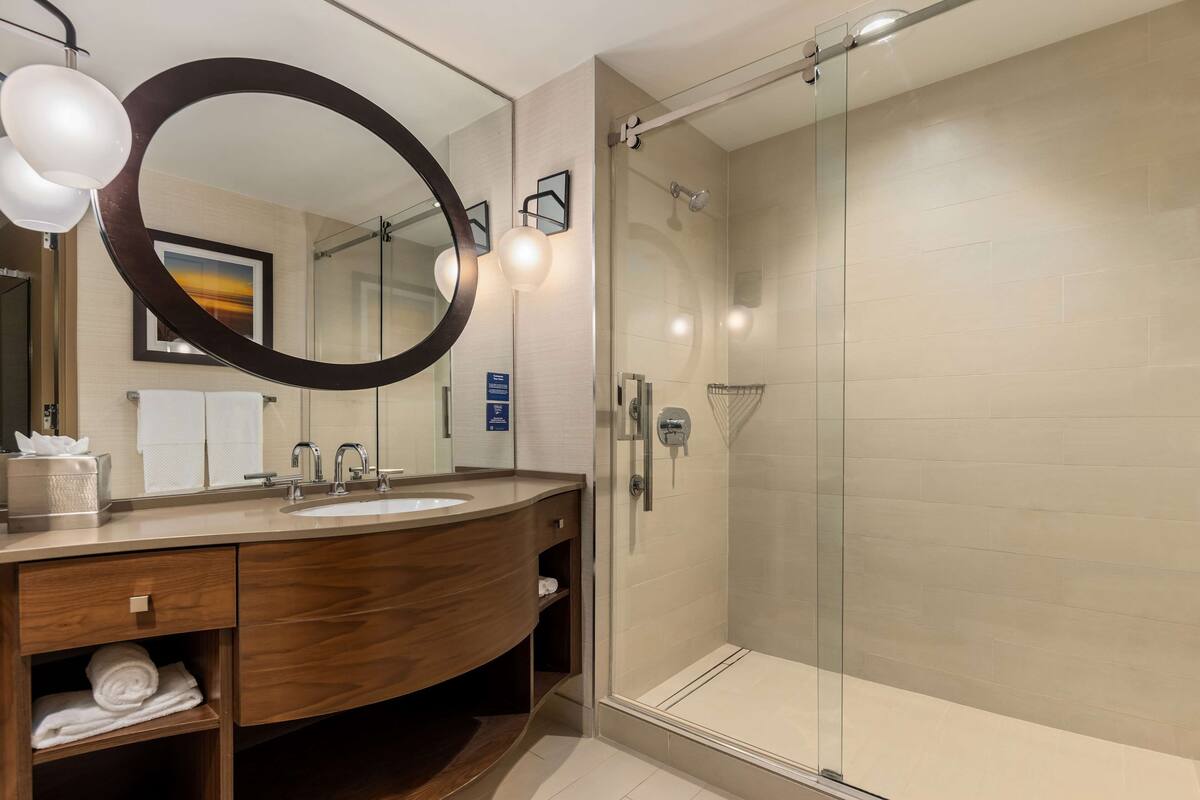 A modern bathroom with a wooden vanity, a large mirror, and a glass-enclosed shower.