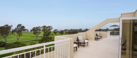 A balcony with a view of a golf course, outdoor seating, and a glass door.