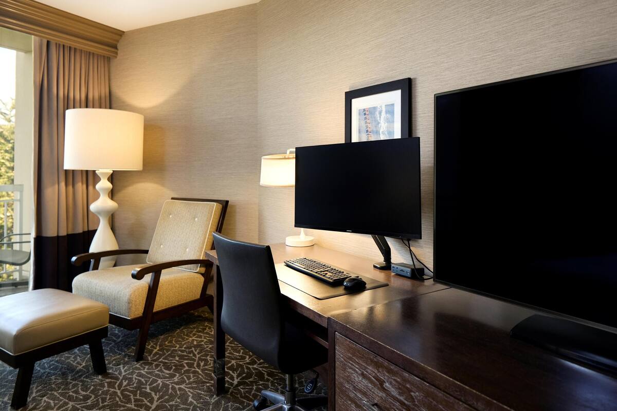 A hotel room with a desk, computer, and television.