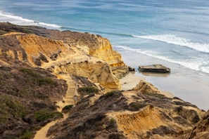 A coastal landscape with a sandy beach, a rocky cliff, and a staircase leading down to the beach. - Hilton La Jolla Torrey Pines (La Jolla)
