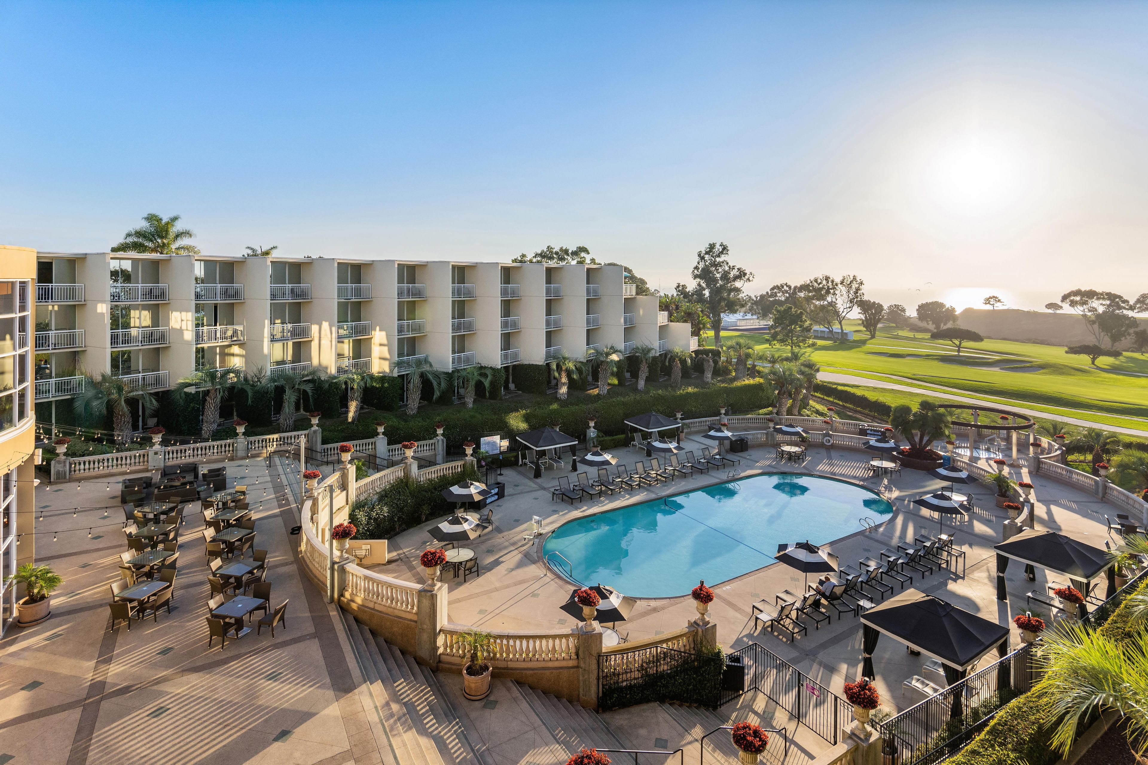 A hotel with a swimming pool, outdoor seating, and a view of the surrounding landscape.