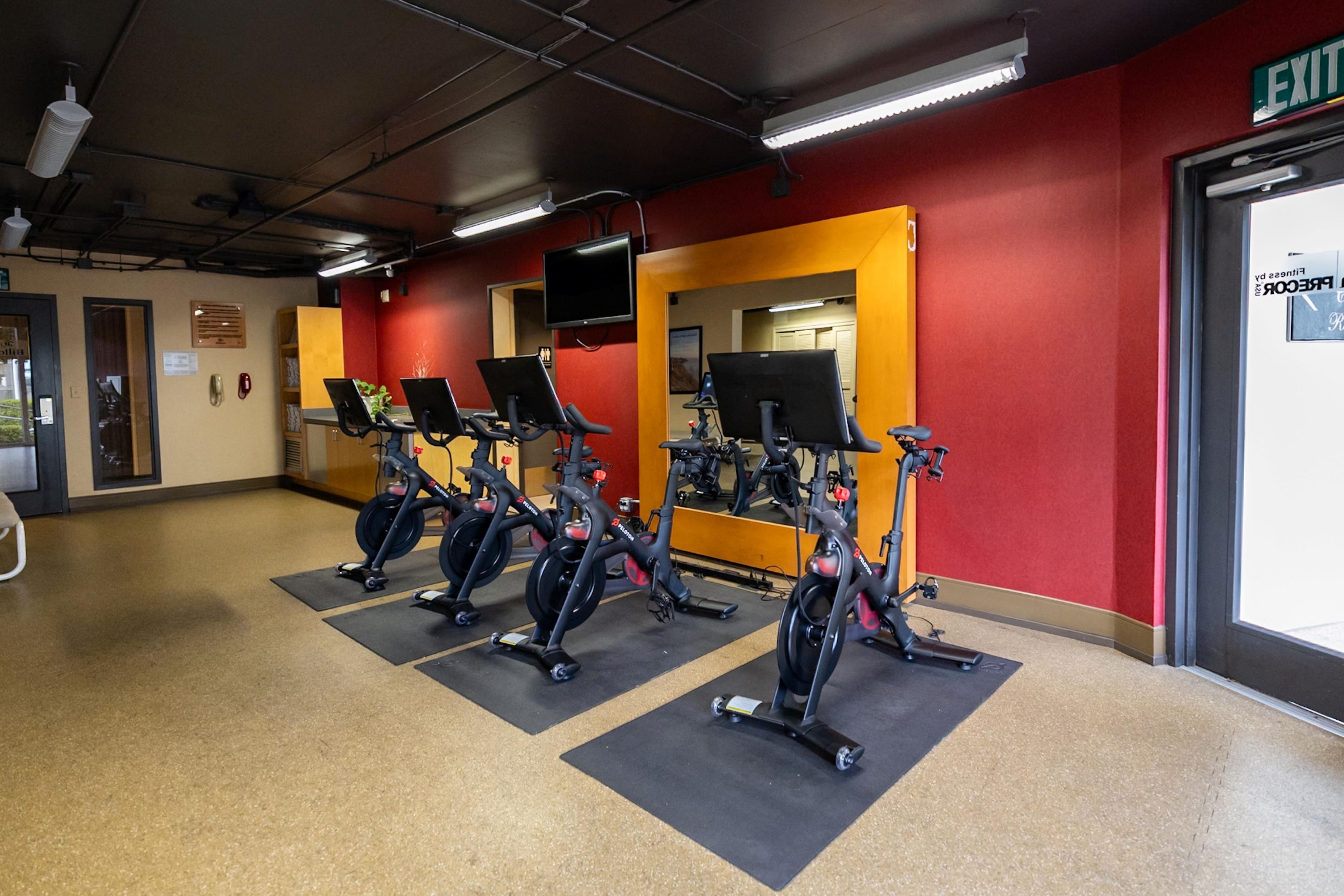 Una palestra con cyclette, un televisore e un cartello di uscita.