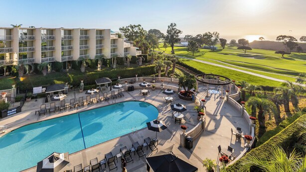 A hotel with a swimming pool, outdoor seating, and a golf course in the background. - Hilton La Jolla Torrey Pines (La Jolla)