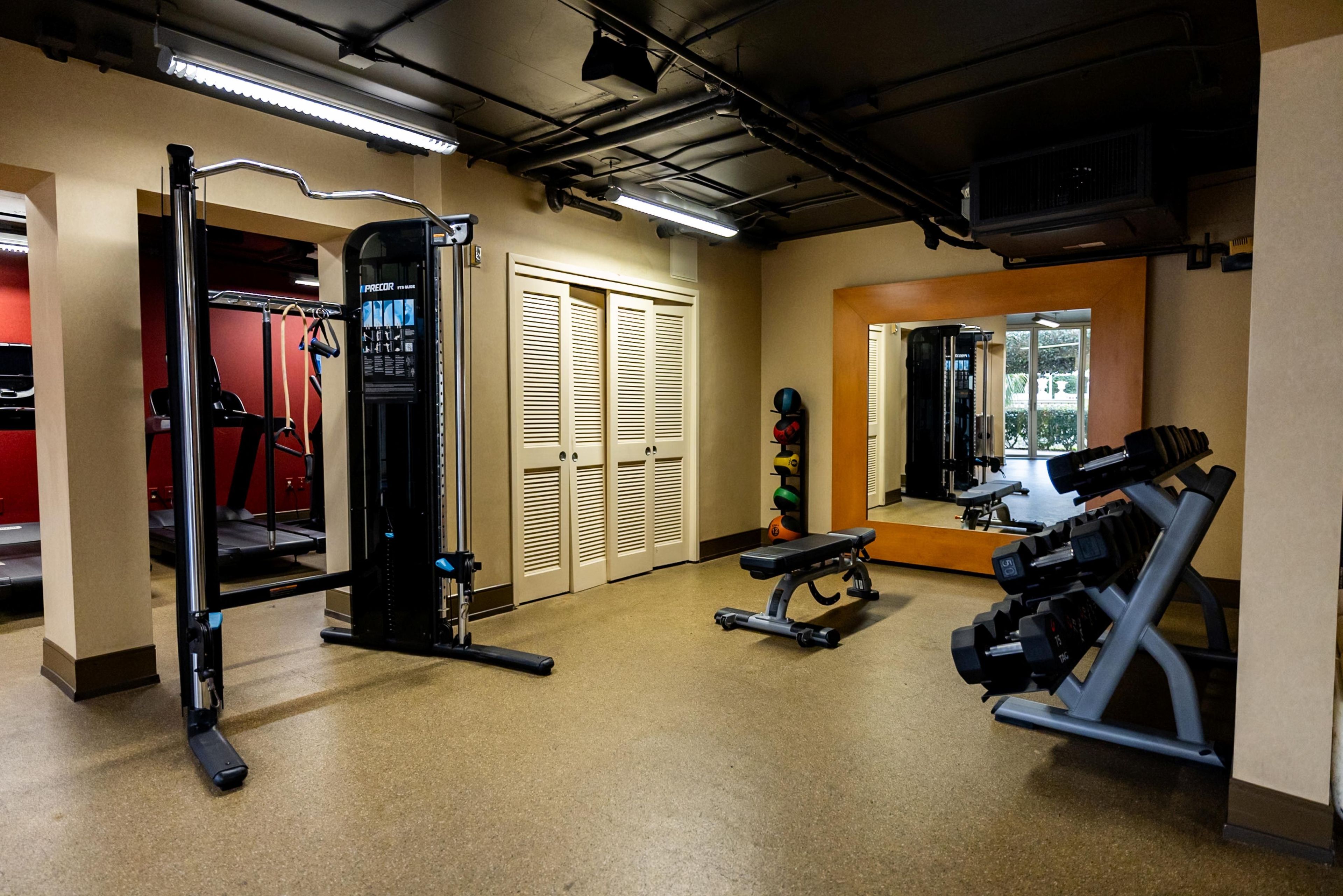 A gym with exercise equipment, a mirror, and a door leading to another room.