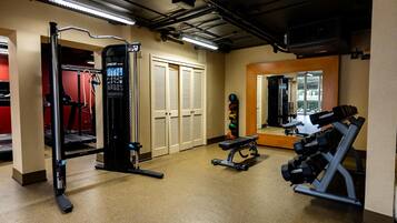 A gym with exercise equipment, a mirror, and a door leading to another room.