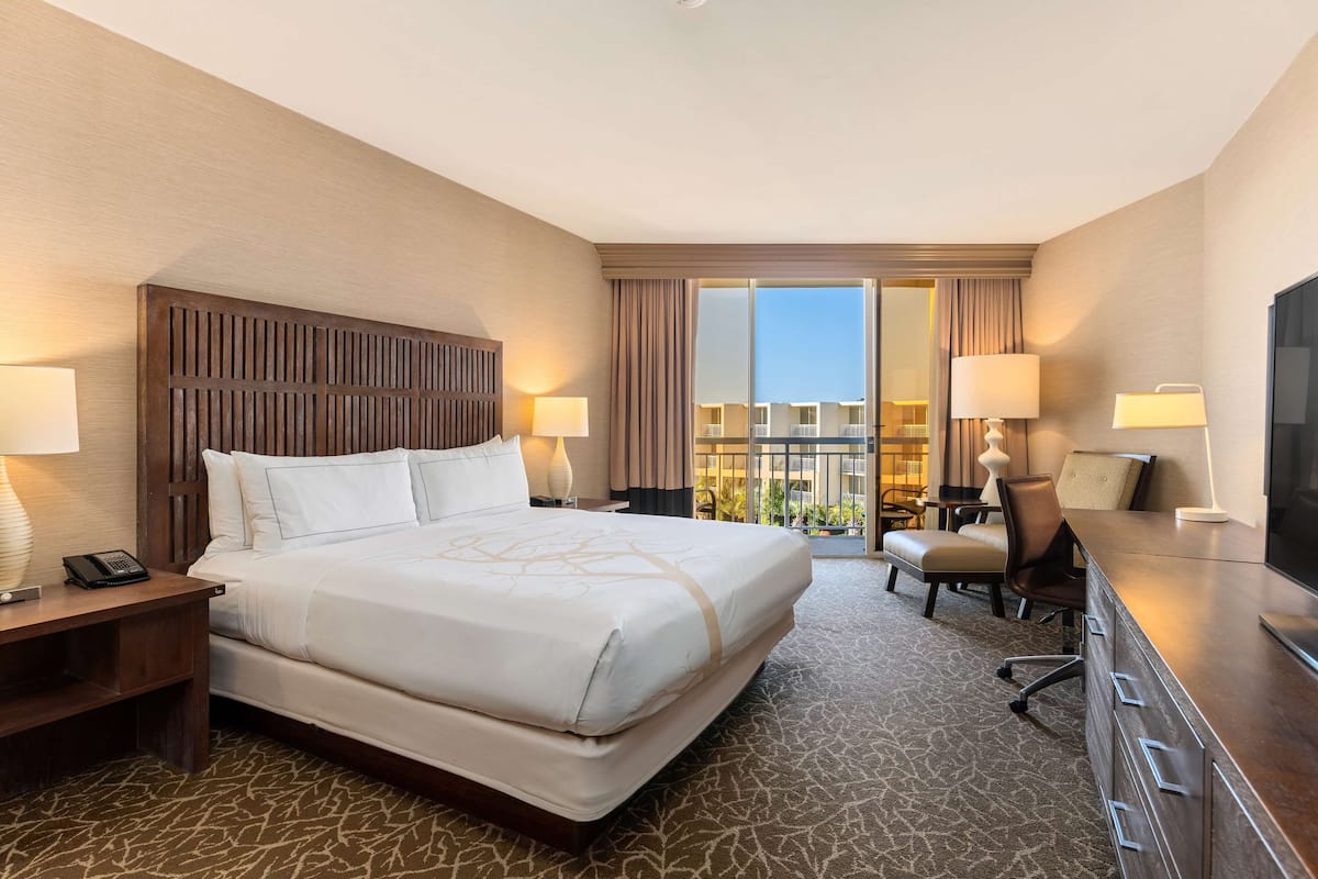 A hotel room with a large bed, a desk with a lamp, a TV, and a view of the outdoors.