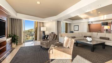 Habitación de hotel moderna con un sofá grande, sillones, una mesa de centro, televisión y un balcón con vistas.