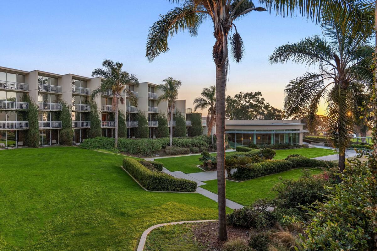A modern hotel with multiple floors, a well-maintained lawn, and palm trees.