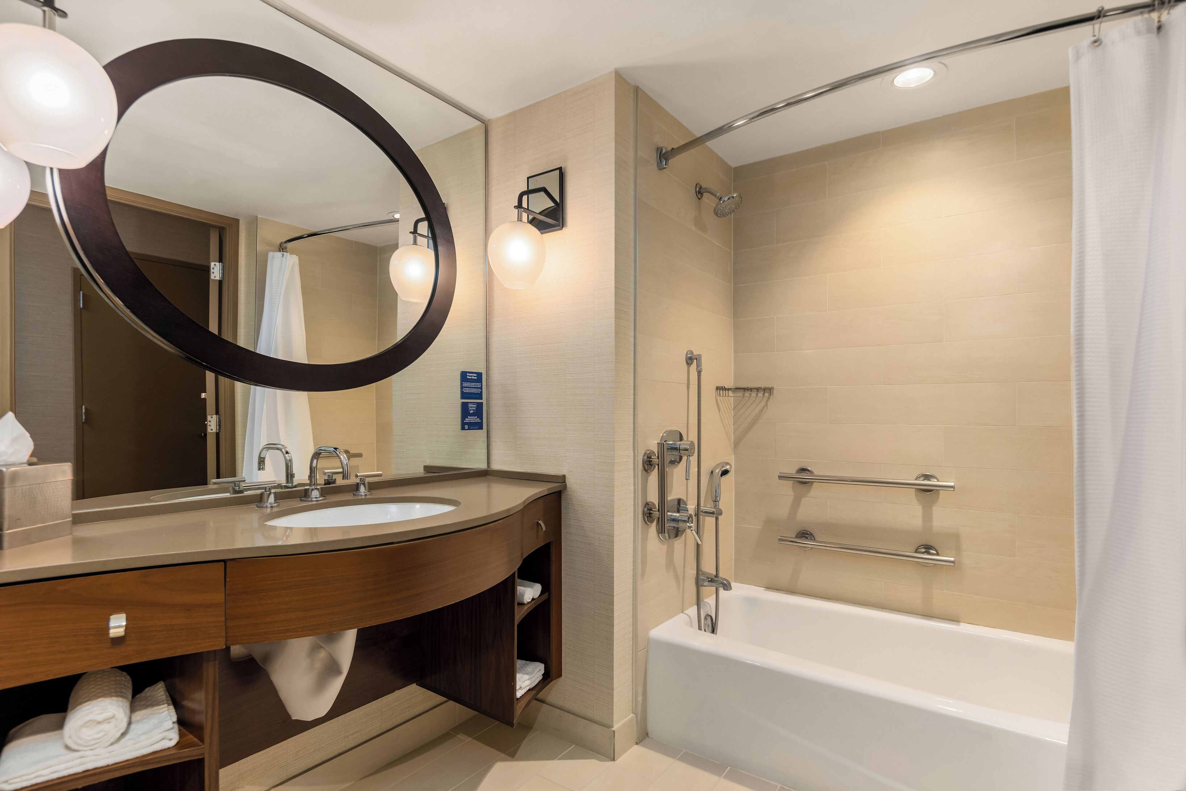 A modern bathroom with a double sink vanity, a large mirror, a shower with a glass door, and a bathtub.
