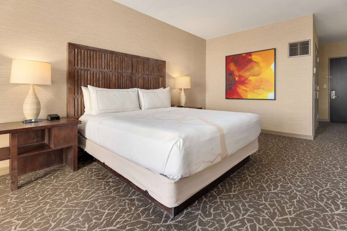 A hotel room with a large bed, two bedside tables with lamps, a wall-mounted artwork, and a patterned carpet.