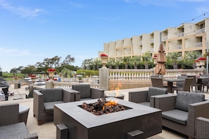 An outdoor seating area with wicker furniture, a fire feature, and a view of a building with balconies. - Hilton La Jolla Torrey Pines (La Jolla)