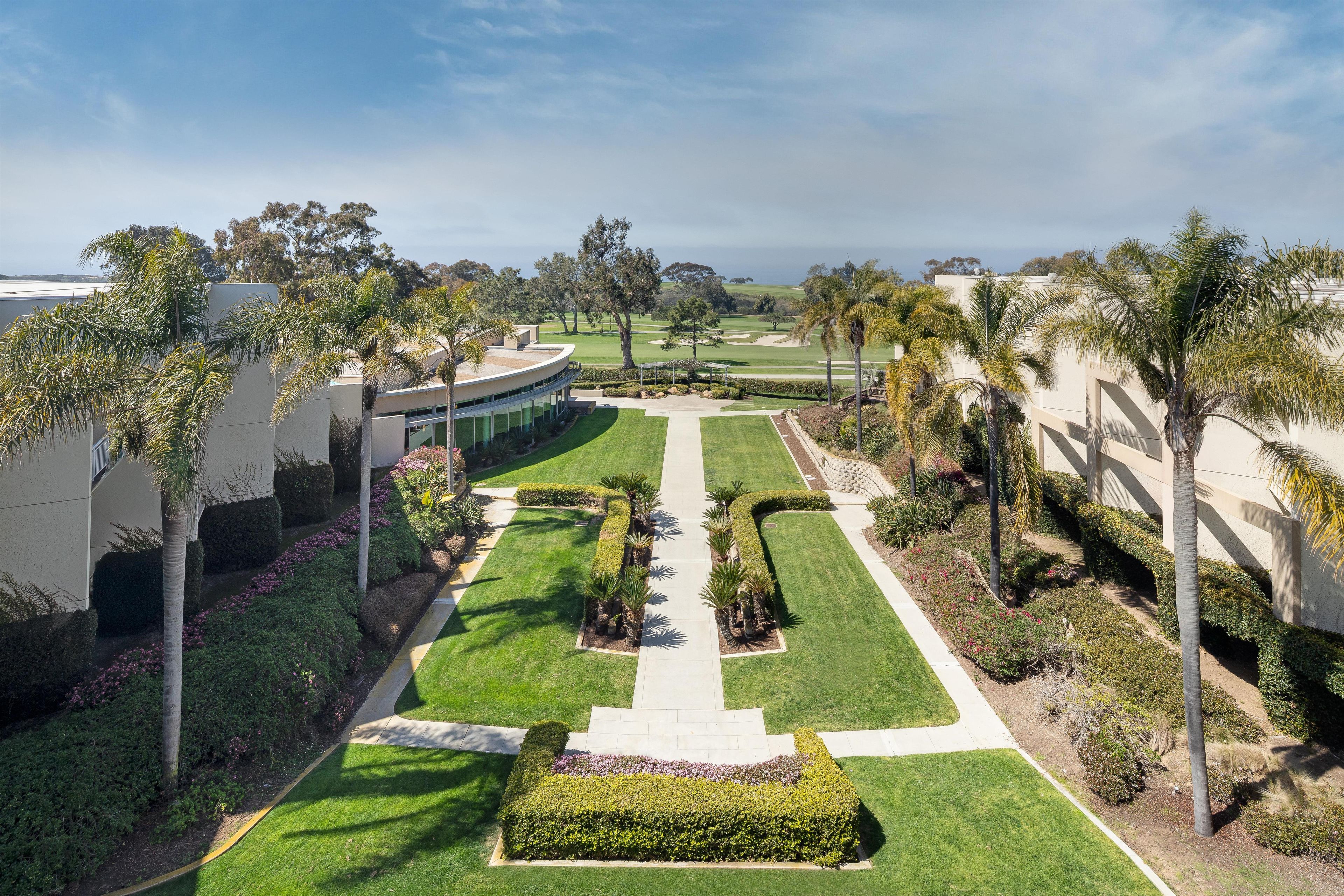 A landscaped area with a golf course in the background, surrounded by palm trees and manicured lawns.