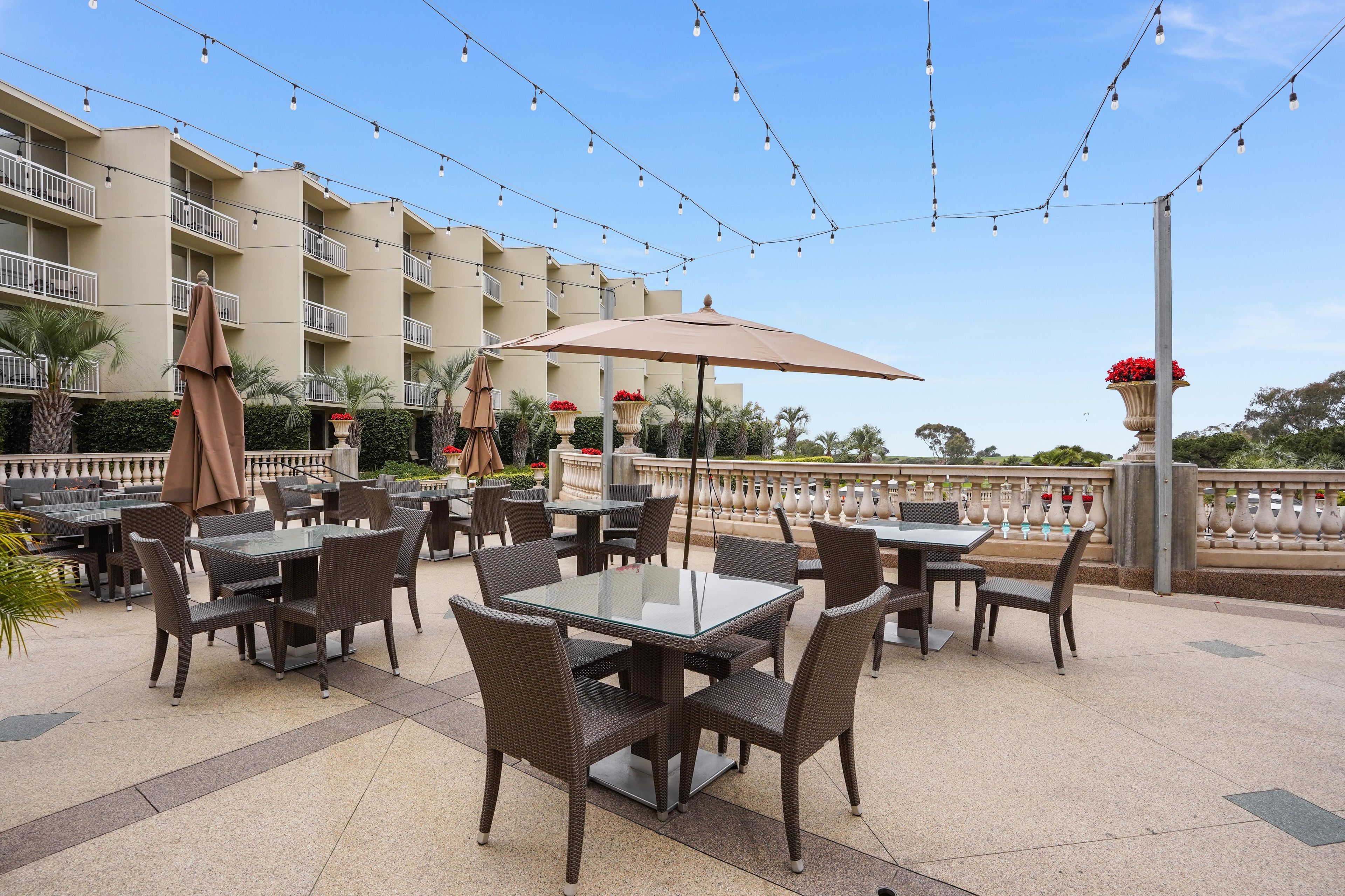 Un espace extérieur aménagé en terrasse, avec des tables et des chaises, des guirlandes lumineuses et une vue sur un immeuble doté de balcons.