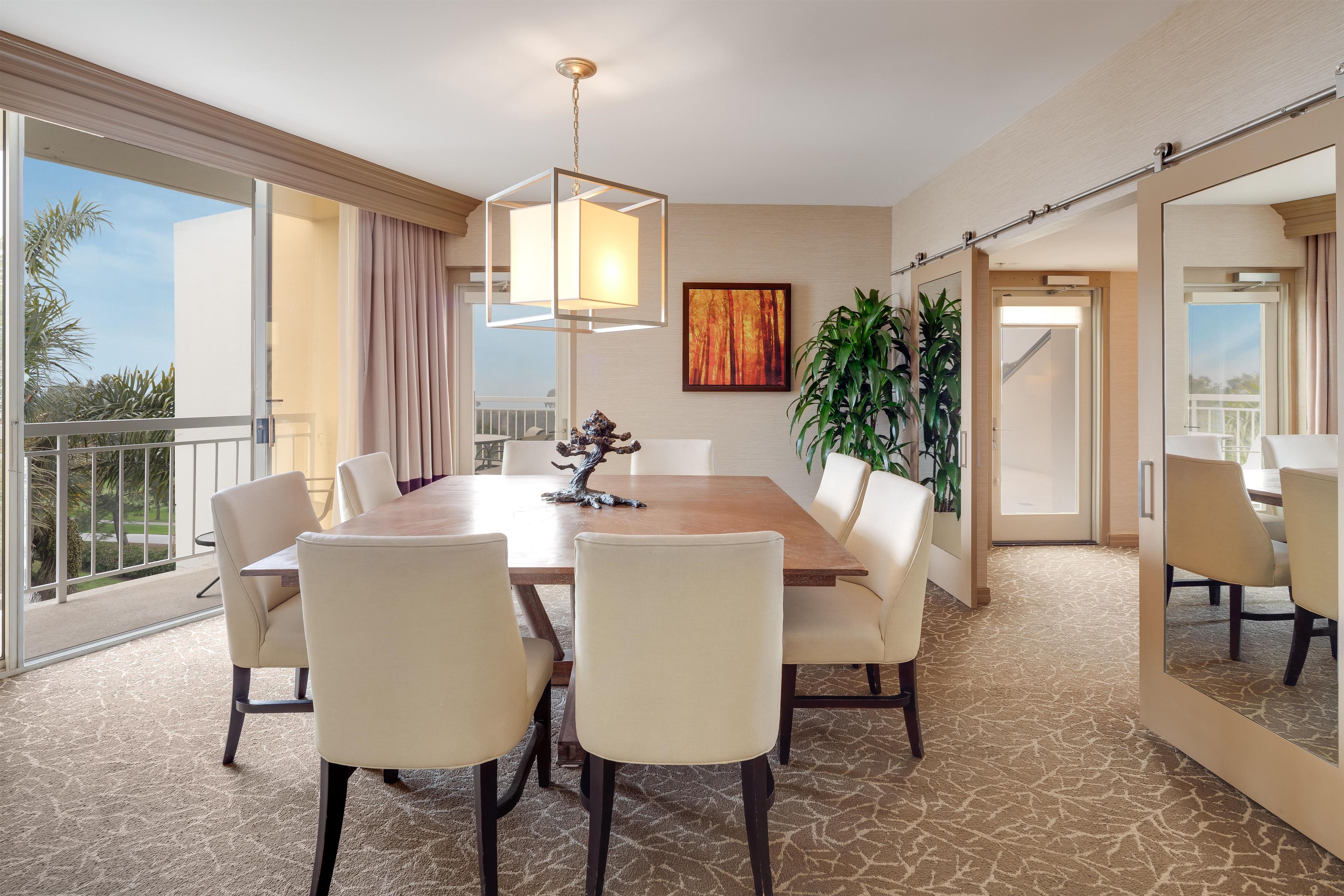 Una sala da pranzo di un hotel con un grande tavolo, sedie, un lampadario, un quadro e una pianta in vaso.