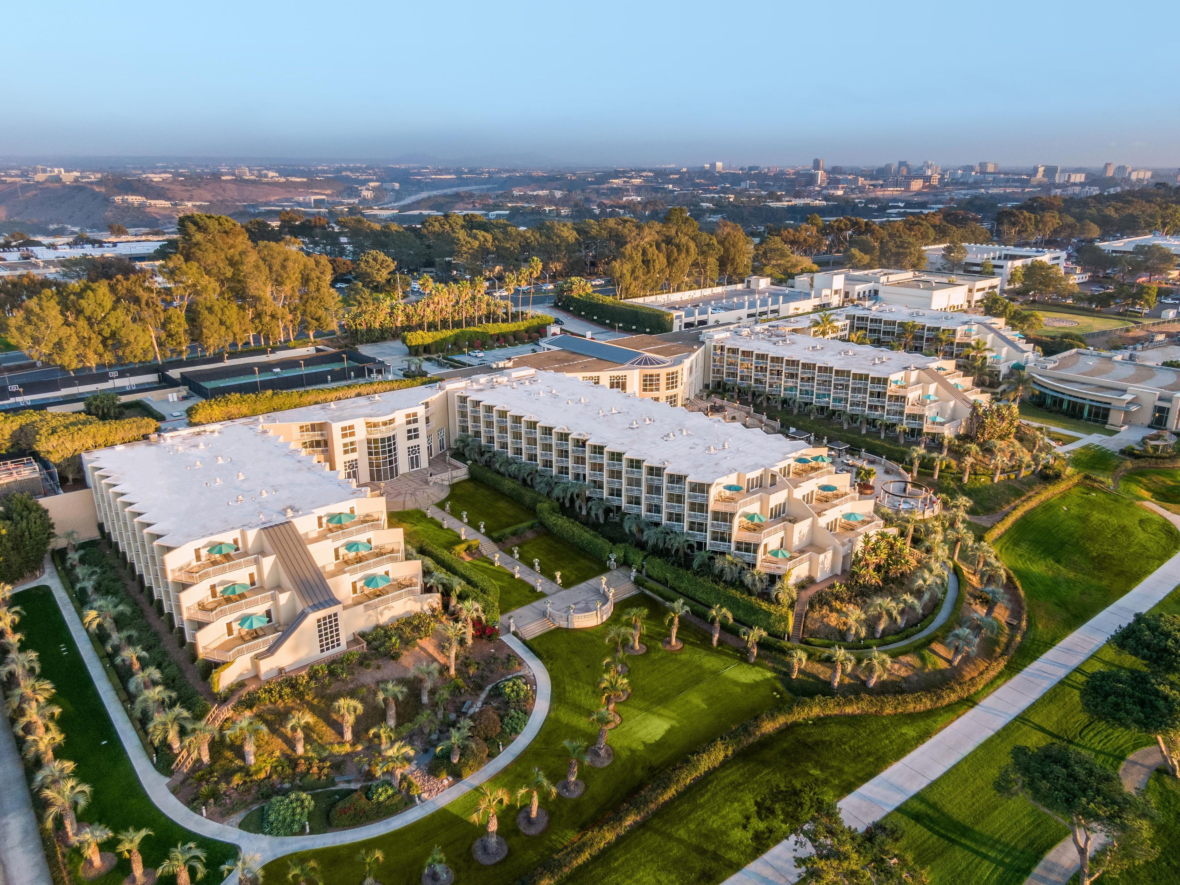 A modern hotel complex with multiple buildings, landscaped gardens, and a clear view of the surrounding cityscape.