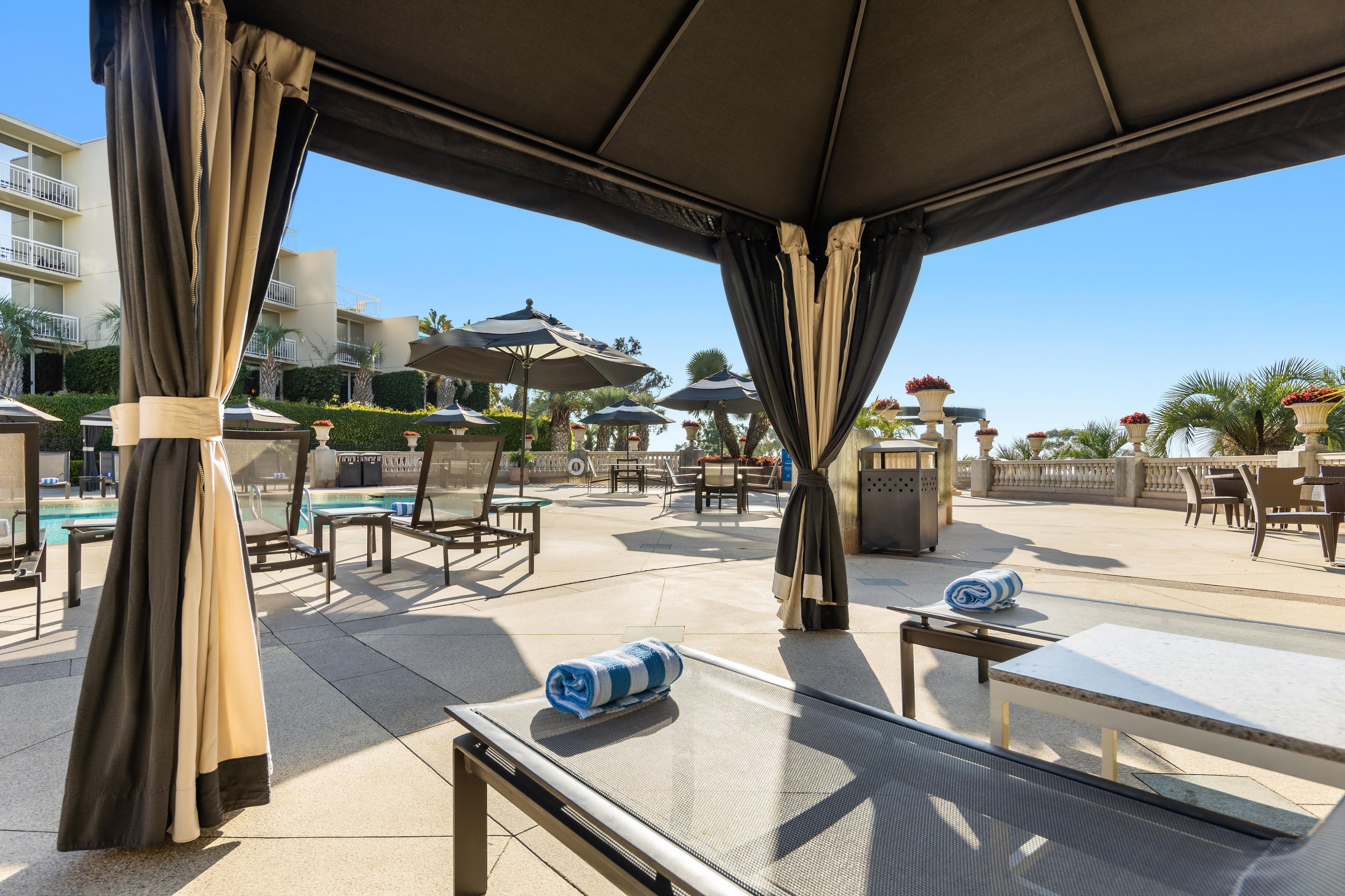 Un área de estar al aire libre con sombrillas, sillones reclinables y una piscina al fondo.