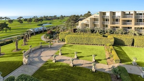 A multi-story hotel with a landscaped garden, a golf course in the background, and a clear sky. - Hilton La Jolla Torrey Pines (La Jolla)