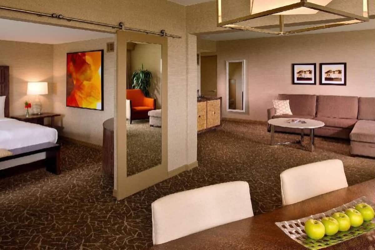 A hotel room with a bed, a dining table with apples, a sofa, and a mirror.