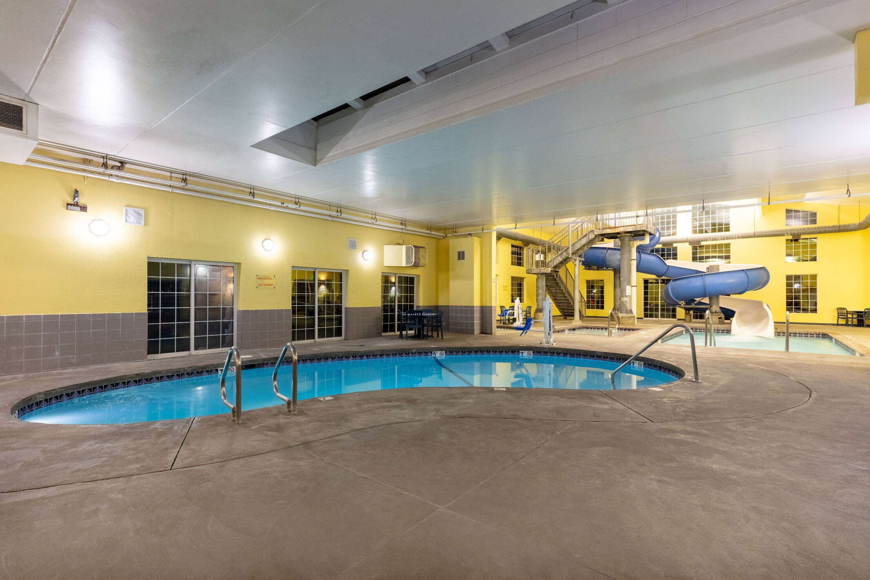 An indoor swimming pool with a blue slide, a staircase, and a seating area.
