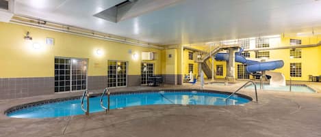 An indoor swimming pool with a blue slide, a staircase, and a seating area.