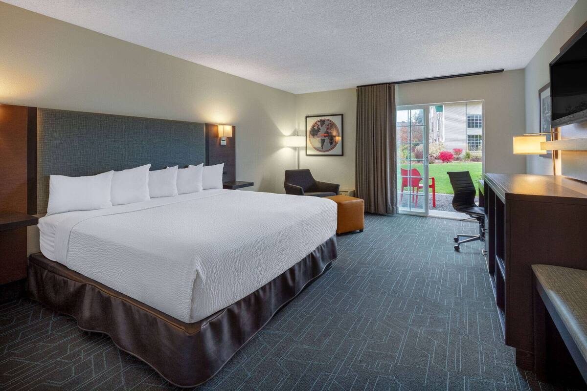 A hotel room with a large bed, a desk, a chair, and a view of the outdoors.