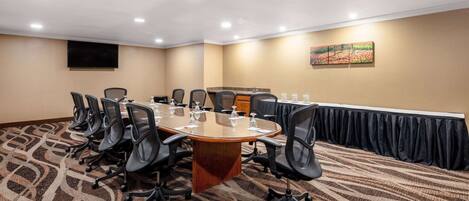 A conference room with a long table, chairs, a TV, and a painting on the wall.