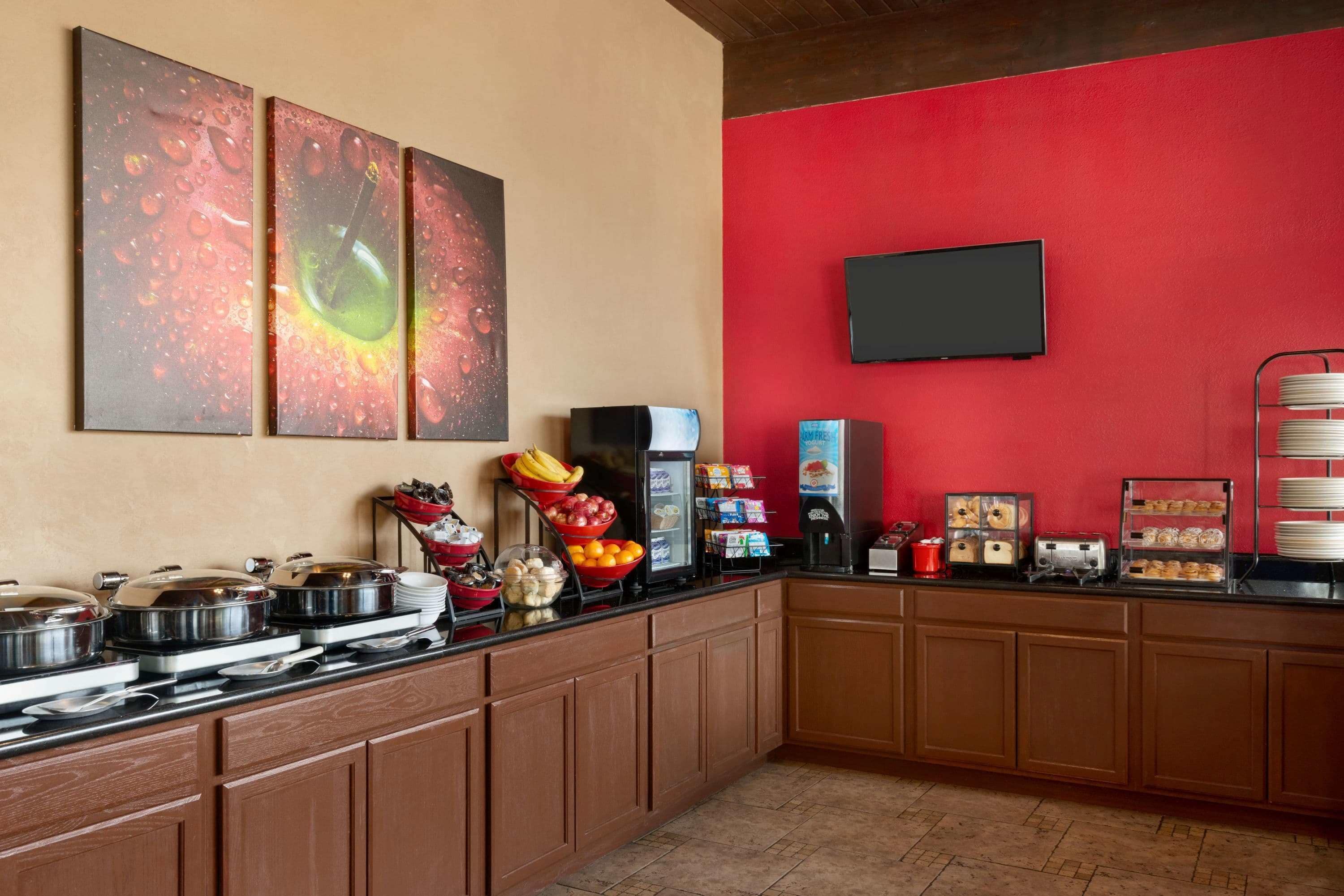 A buffet setup with various food items and a flat-screen TV mounted on a red wall.