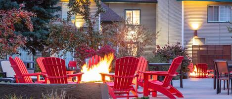 A patio area with red Adirondack chairs around a fire pit, a stone wall, and a building in the background.