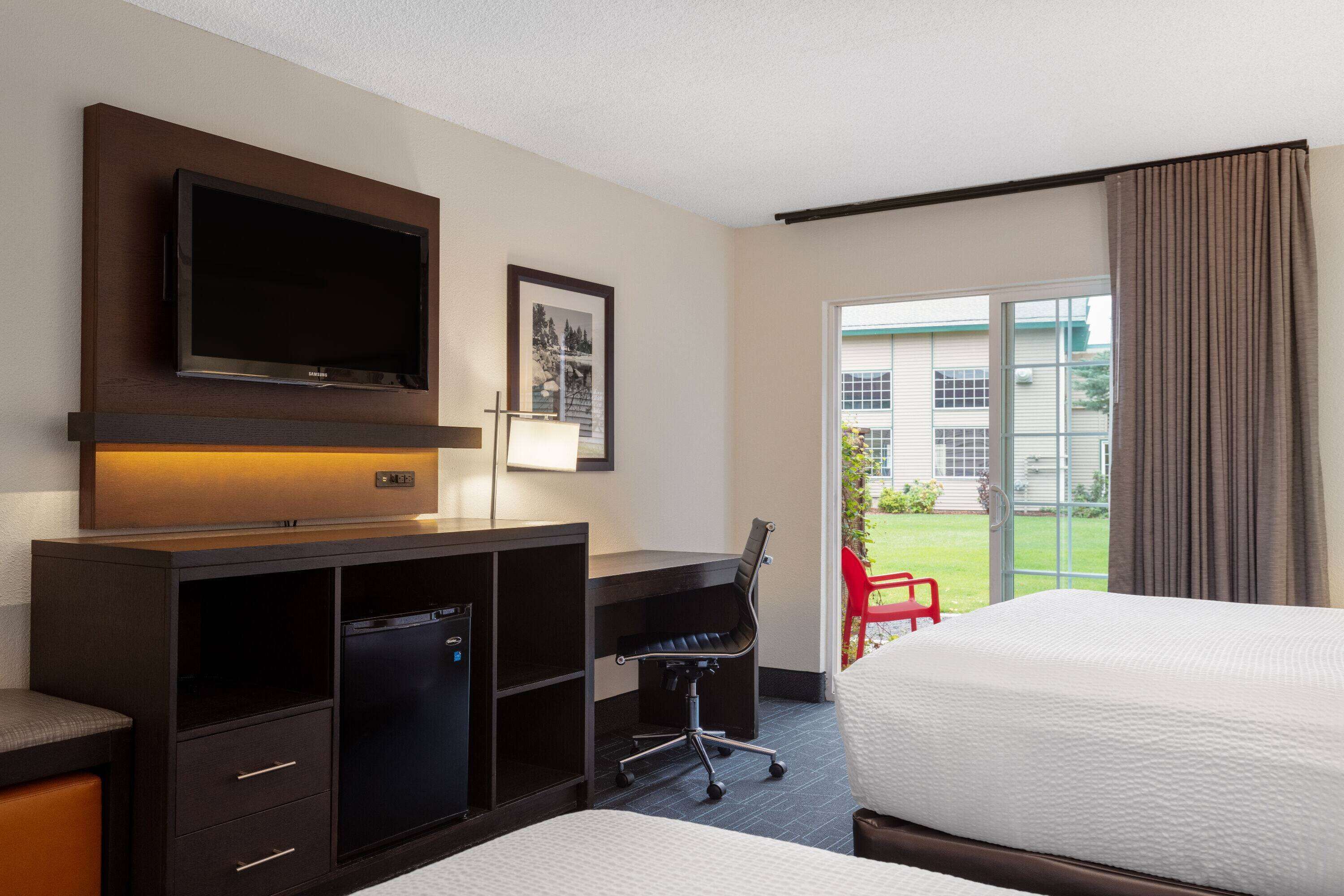 Quarto de hotel com cama, escrivaninha, cadeira, televisão e janela com cortinas.