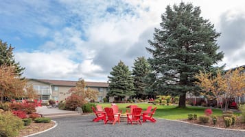 Un patio con sillas Adirondack rojas, un árbol grande y un edificio al fondo.