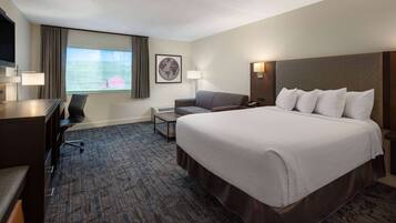 A hotel room with a large bed, a desk, a chair, a sofa, a TV, and a window with curtains.