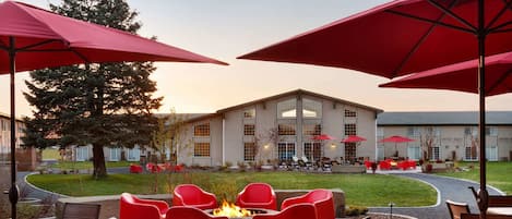 Un patio al aire libre con sillas y mesas rojas, un hogar para la chimenea y sombrillas rojas.