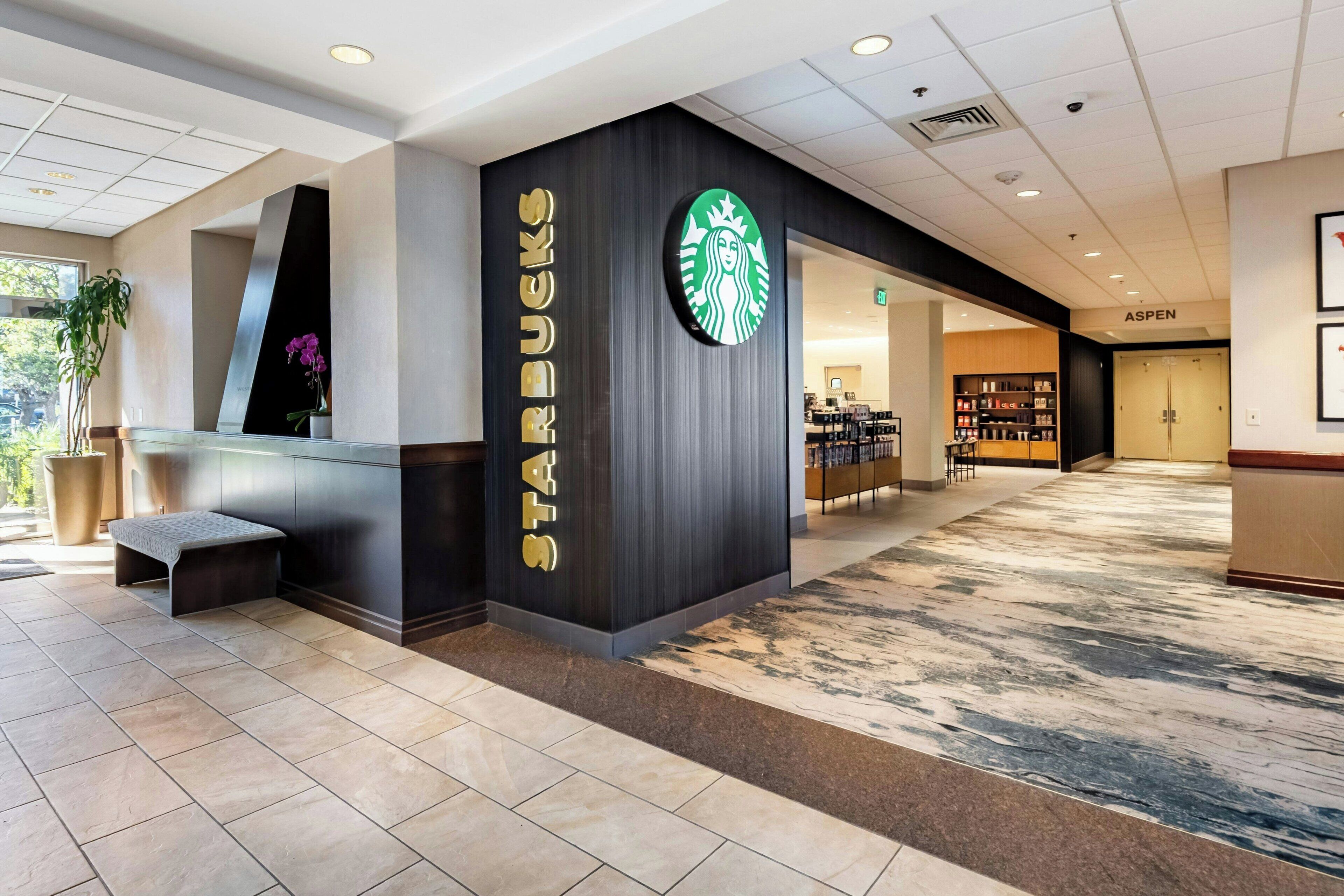 Una tienda Starbucks con un diseño moderno, que presenta un logotipo grande en la pared y una zona de estar con un banco.