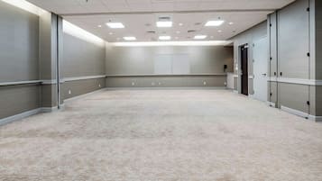 Un salón de conferencias amplio y luminoso, con suelo alfombrado, ventanas grandes y una puerta que da a otra habitación.