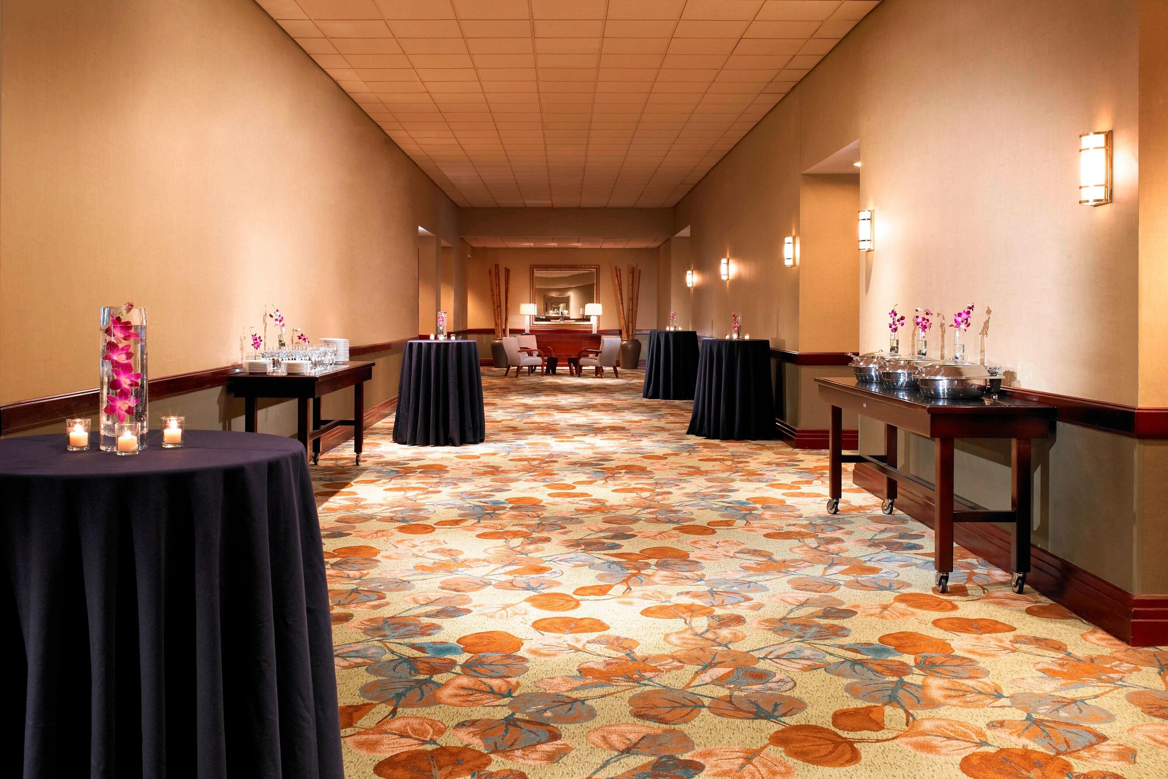 A hotel corridor with round tables, chairs, and a carpeted floor.